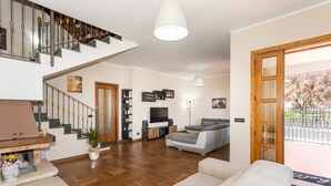 A spacious living area with a staircase, a sofa, a TV, and a wooden door leading outside. - Villa 'Il Vulcano di Milo' (Milo)