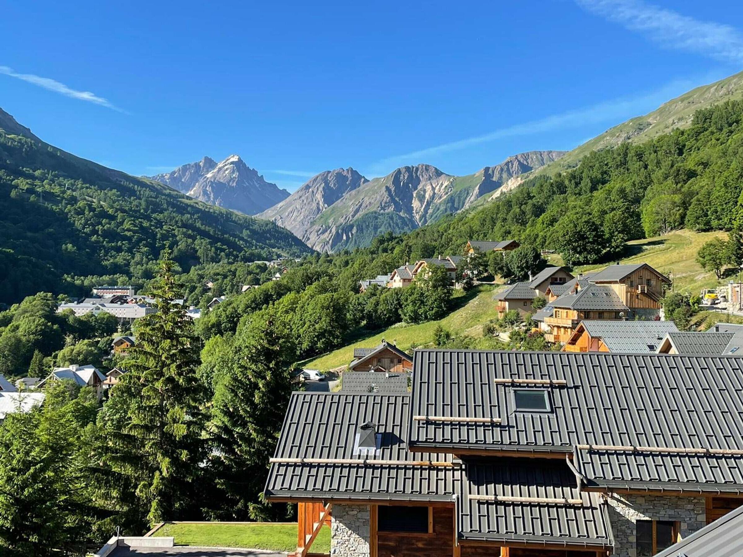 A mountain village with traditional wooden houses, a clear sky, and a backdrop of rugged mountains.