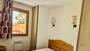 Un dormitorio con cama de madera, ventana con cortinas, calefactor en la pared y vista a un edificio de madera en el exterior.
