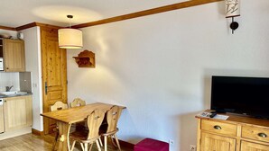 Un espacio habitable compacto con una mesa de comedor de madera, sillas, un televisor y una pequeña cocina.
