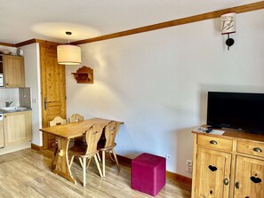A compact living space with a wooden dining table, chairs, a television, and a small kitchen area. - Cozy apartment - 4 guests (Valloire)