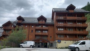 Un edificio a più piani in legno con balconi, un'area di parcheggio e due furgoni bianchi parcheggiati davanti.