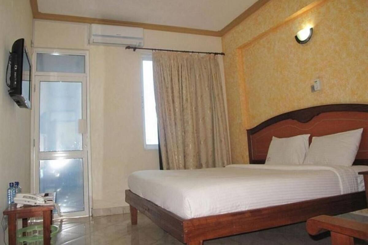 Une chambre d’hôtel avec un lit, une télévision, une fenêtre avec des rideaux et un ventilateur de plafond.