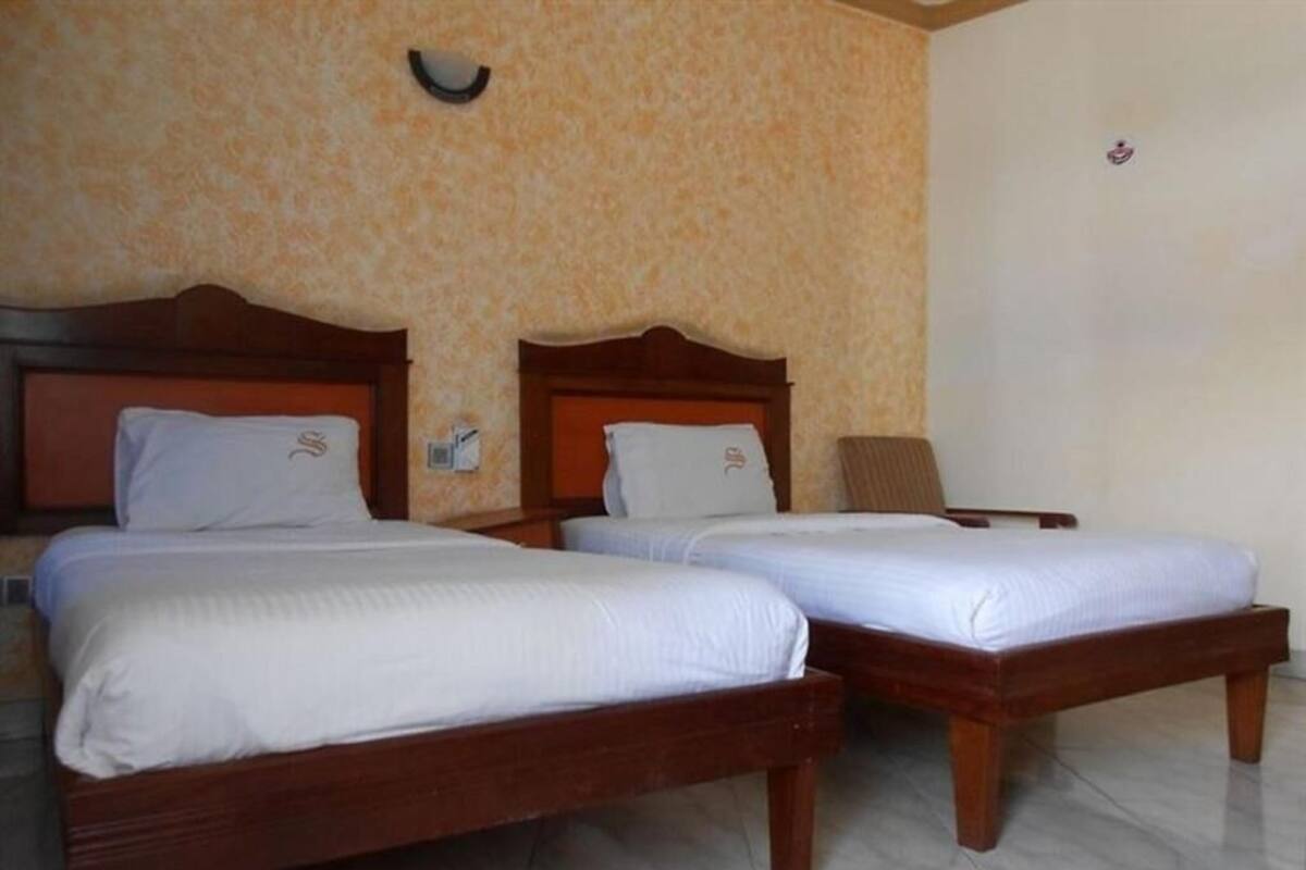Deux lits en bois, recouverts de draps blancs, se trouvent dans une pièce aux murs décorés de motifs et au sol carrelé.
