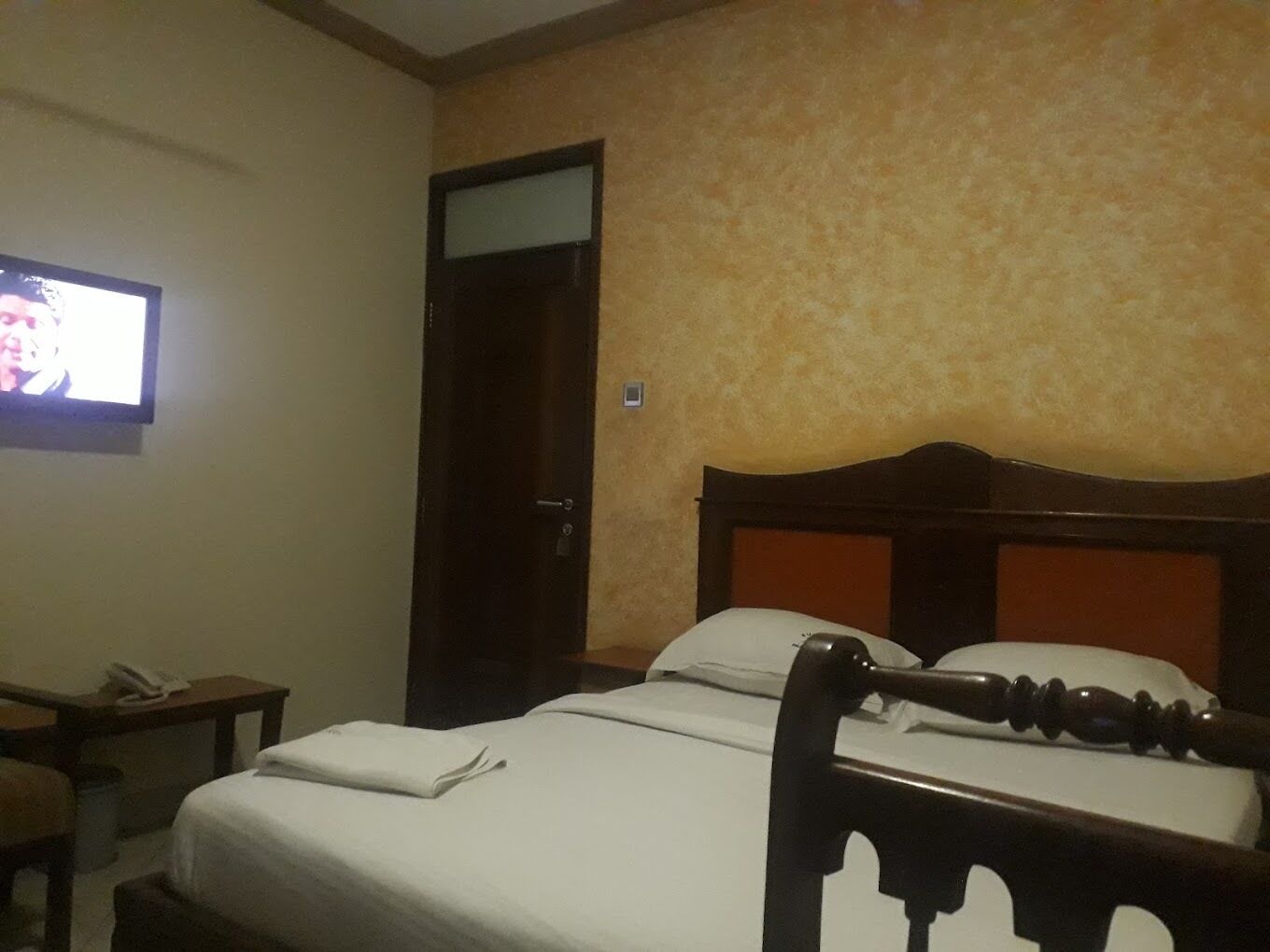 A hotel room with a bed, a television on the wall, and a door.