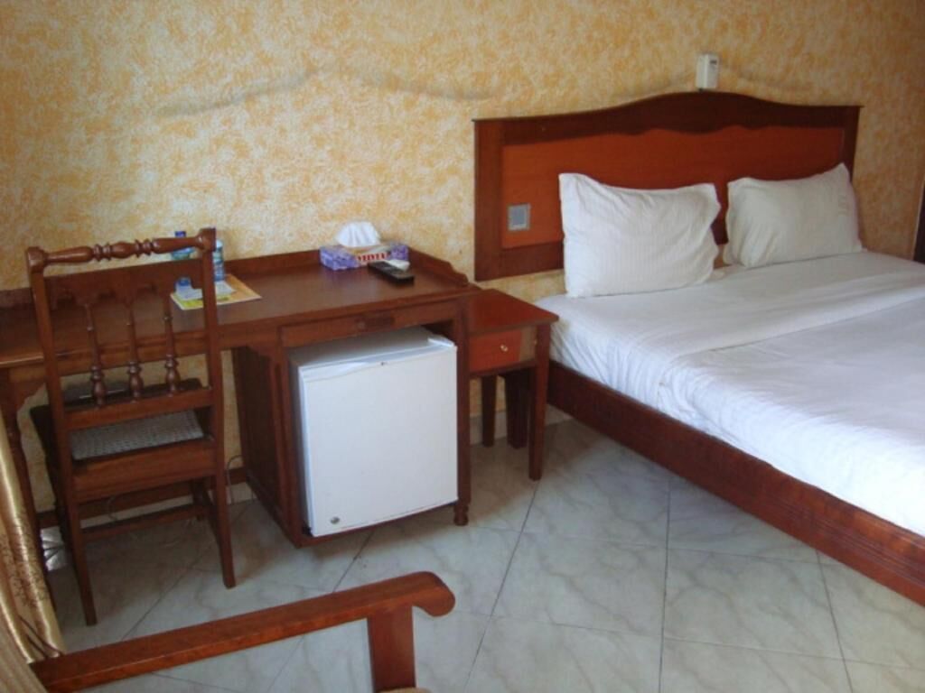 A bedroom with a bed, a wooden desk with a small refrigerator, and a chair.