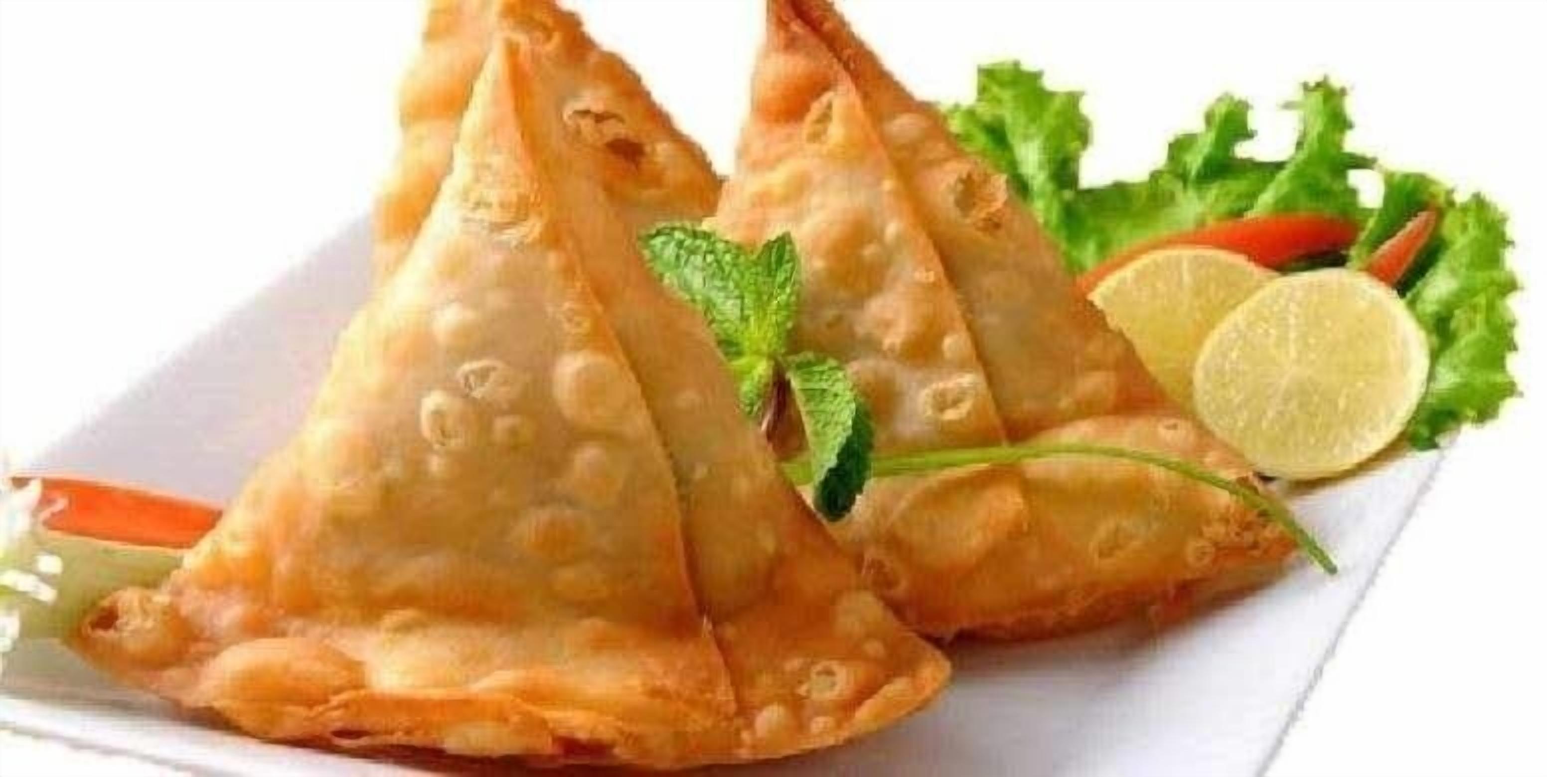 Tres pasteles triangulares sobre un plato blanco, adornados con menta y una rodaja de lima.