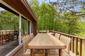 A wooden deck with a table and chairs, overlooking a forested area.