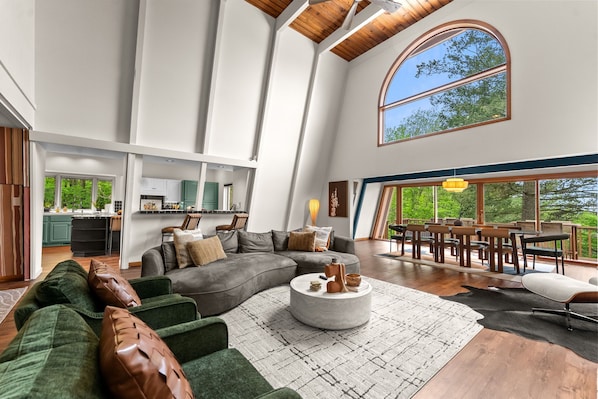 A spacious living area with a large curved sofa, a round coffee table, and a view of a dining area through a large arched window.