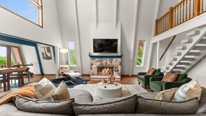 Un salón espacioso con chimenea de piedra, un televisor grande montado encima y una escalera con barandillas de madera.