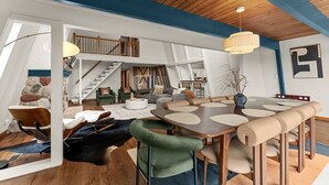 Un loft espacioso con techo alto, comedor con mesa y sillas grandes, escalera y zona de estar acogedora con sofás y una mesa de centro.
