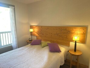 A bedroom with a bed, two bedside lamps, a wooden headboard with a map, and a window with curtains. - Ideal duplex - 6 guests (Valloire)