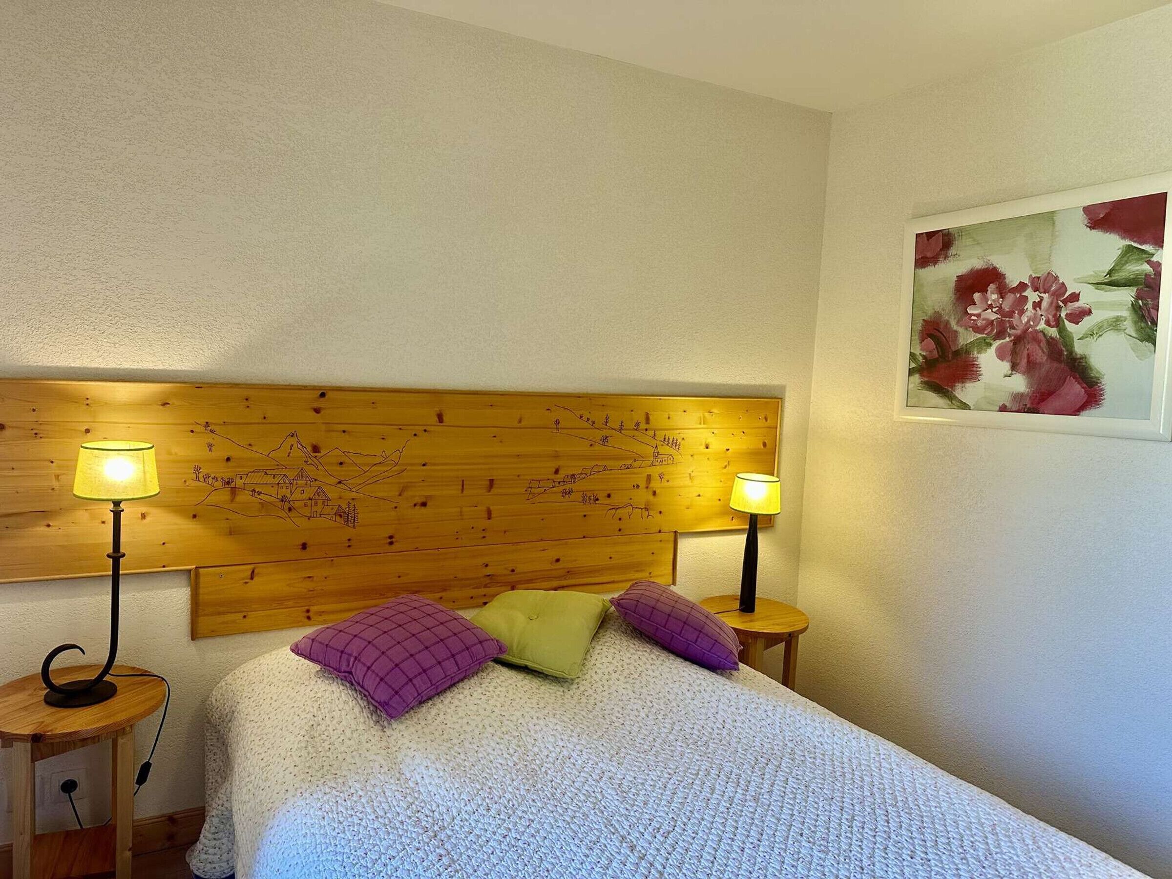 Un lit avec une tête de lit en bois, deux lampes de chevet et un tableau floral accroché au mur.