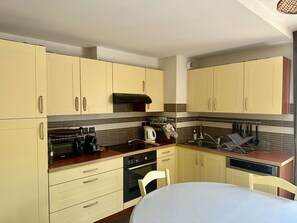 Een compacte keuken met beige kastjes, een zwarte kookplaat en een witte eettafel.