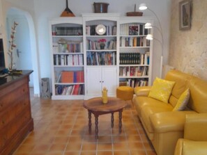 Un salon avec un canapé jaune, une table basse en bois et une bibliothèque blanche remplie de livres.