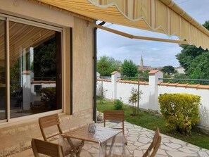 A patio with a table and chairs, a covered area, and a view of a building with a tower. - House by the water, pets welcome - 4 guests (Bergerac)