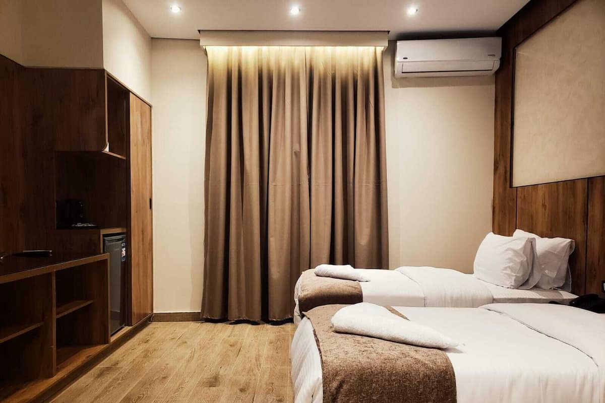 Habitación de hotel con dos camas, suelo de madera, un armario, un equipo de aire acondicionado y una cortina.