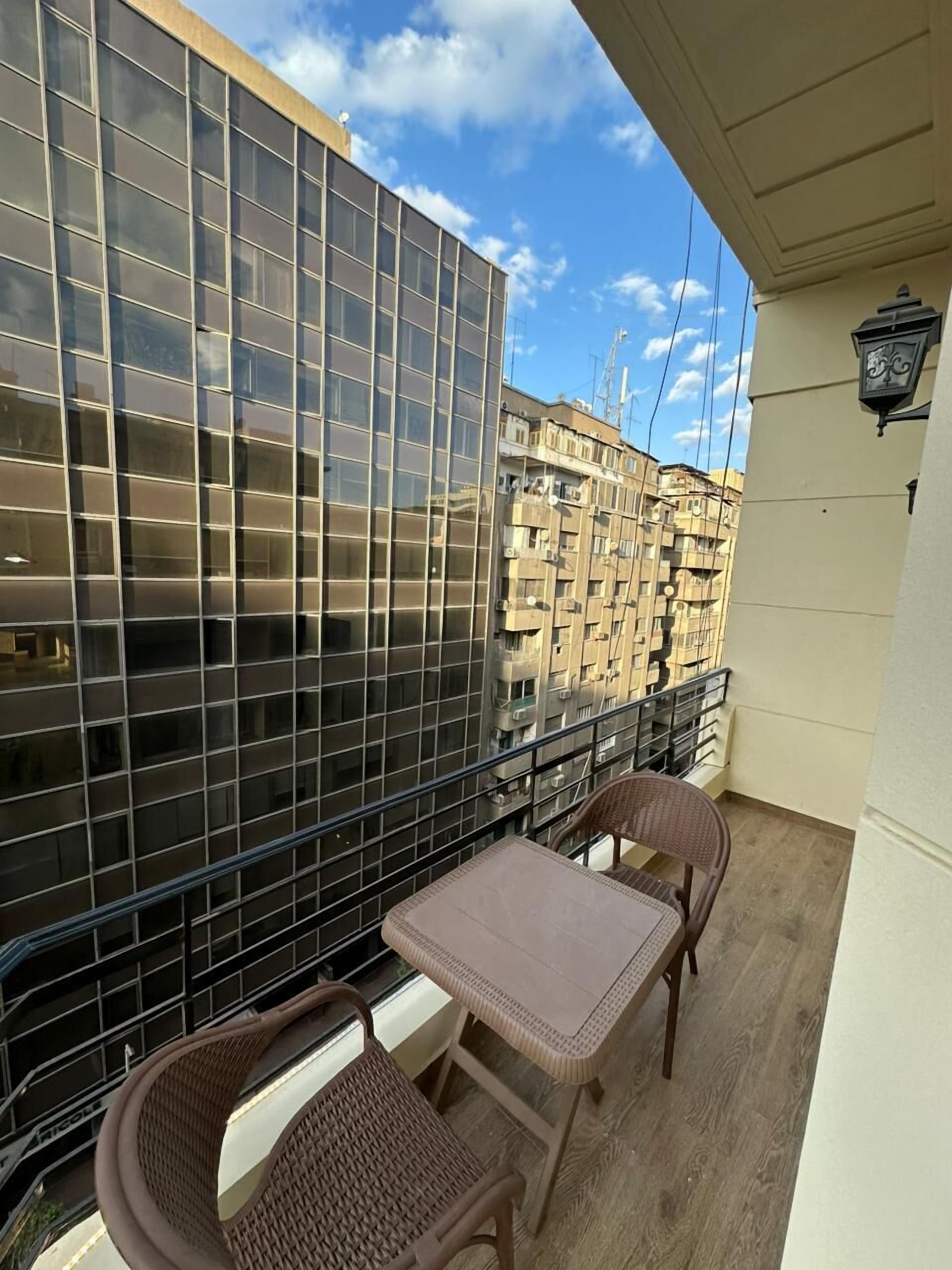Un balcon doté d’une paroi en verre, de deux fauteuils en osier, d’une petite table et d’une lampe.