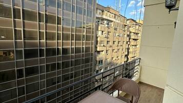 Un balcon doté d’une paroi en verre, de deux fauteuils en osier, d’une petite table et d’une lampe.