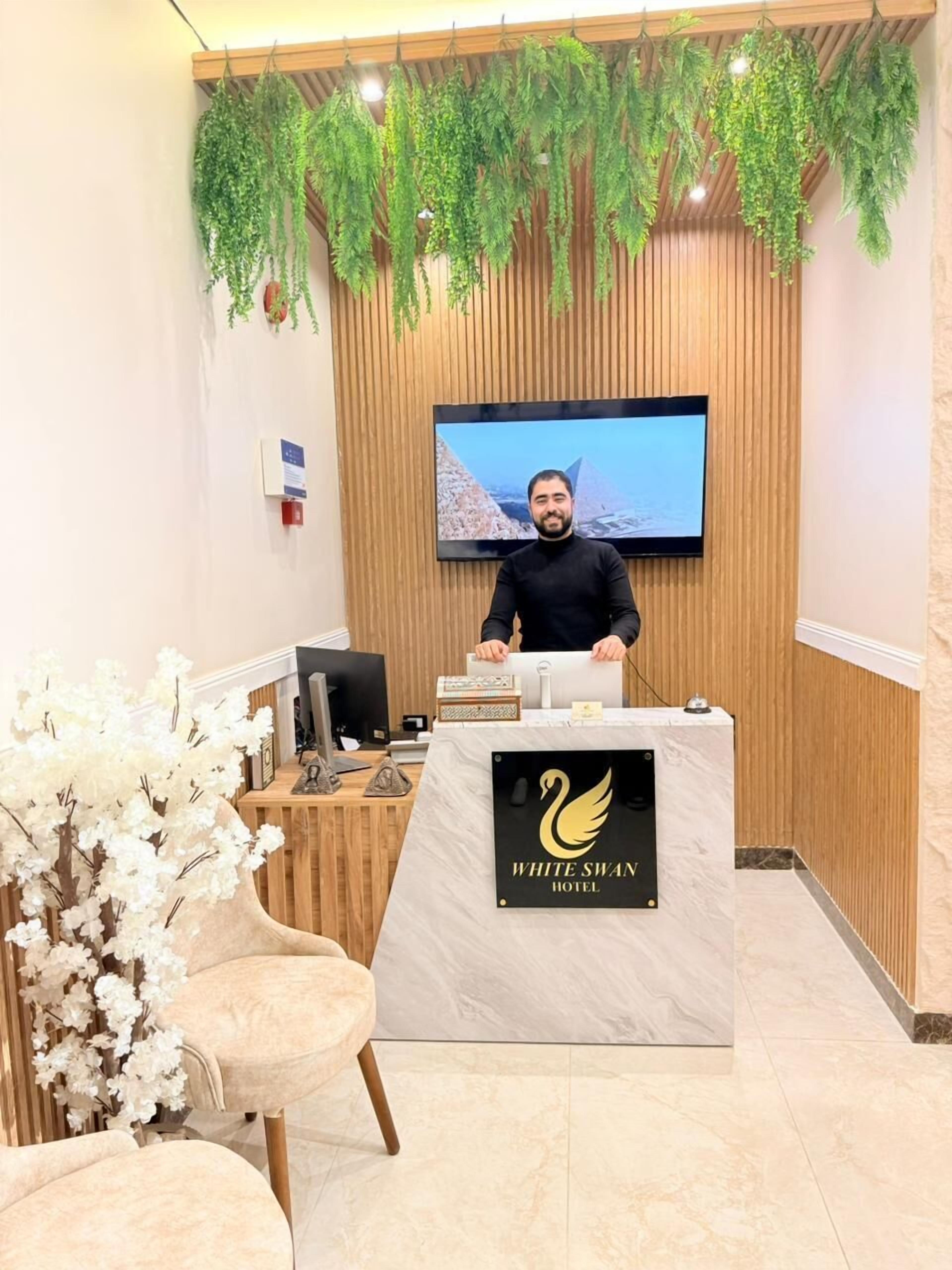 Un comptoir d’accueil doté d’un écran de télévision, du logo de l’hôtel White Swan et d’un mur en bois orné de plantes suspendues.
