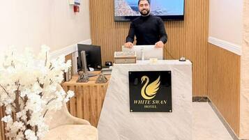 A reception desk with a television screen, a logo for White Swan Hotel, and a wooden wall with hanging plants.