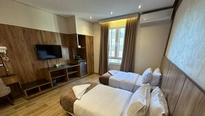 A hotel room with a large bed, a TV mounted on the wall, a small desk, and a window with curtains. - white swan hotel (Cairo)