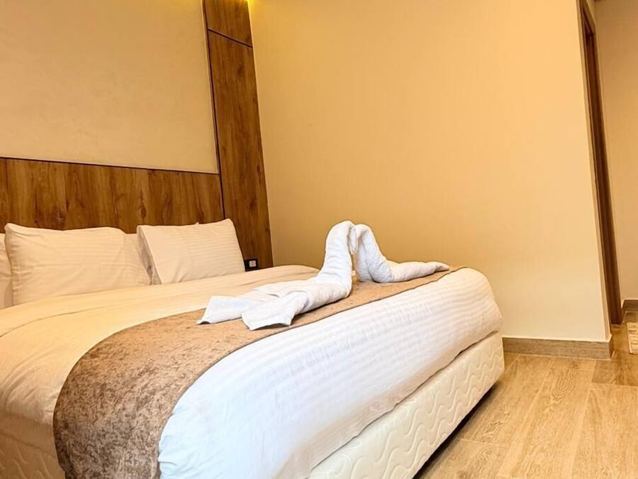 Habitación de hotel moderna con una cama grande, cabecera de madera y una luz ambiental cálida.