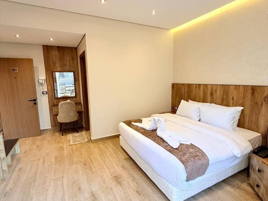 A modern hotel room with a large bed, wooden headboard, and a small bedside table.
