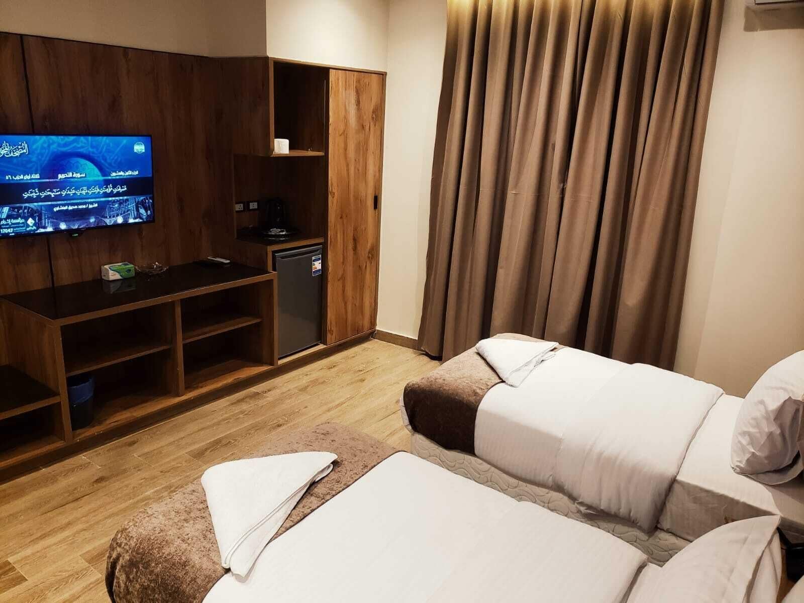 Quarto de hotel com televisão, uma kitchenette pequena, cama e janela com cortinas.