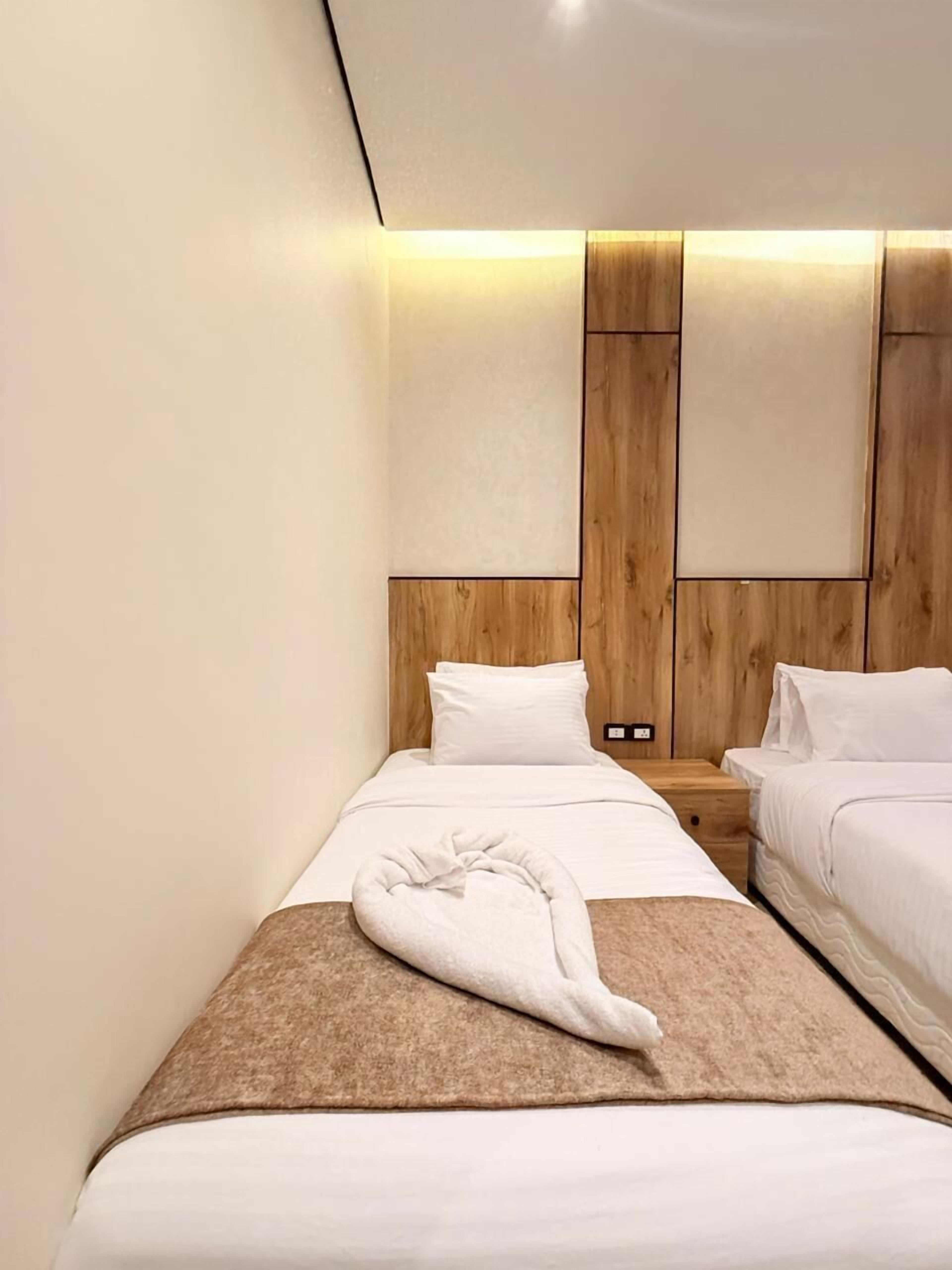 Ein Hotelzimmer mit einem Holzkopfteil, zwei Betten, einem Nachttisch und einem Handtuch auf dem Bett.