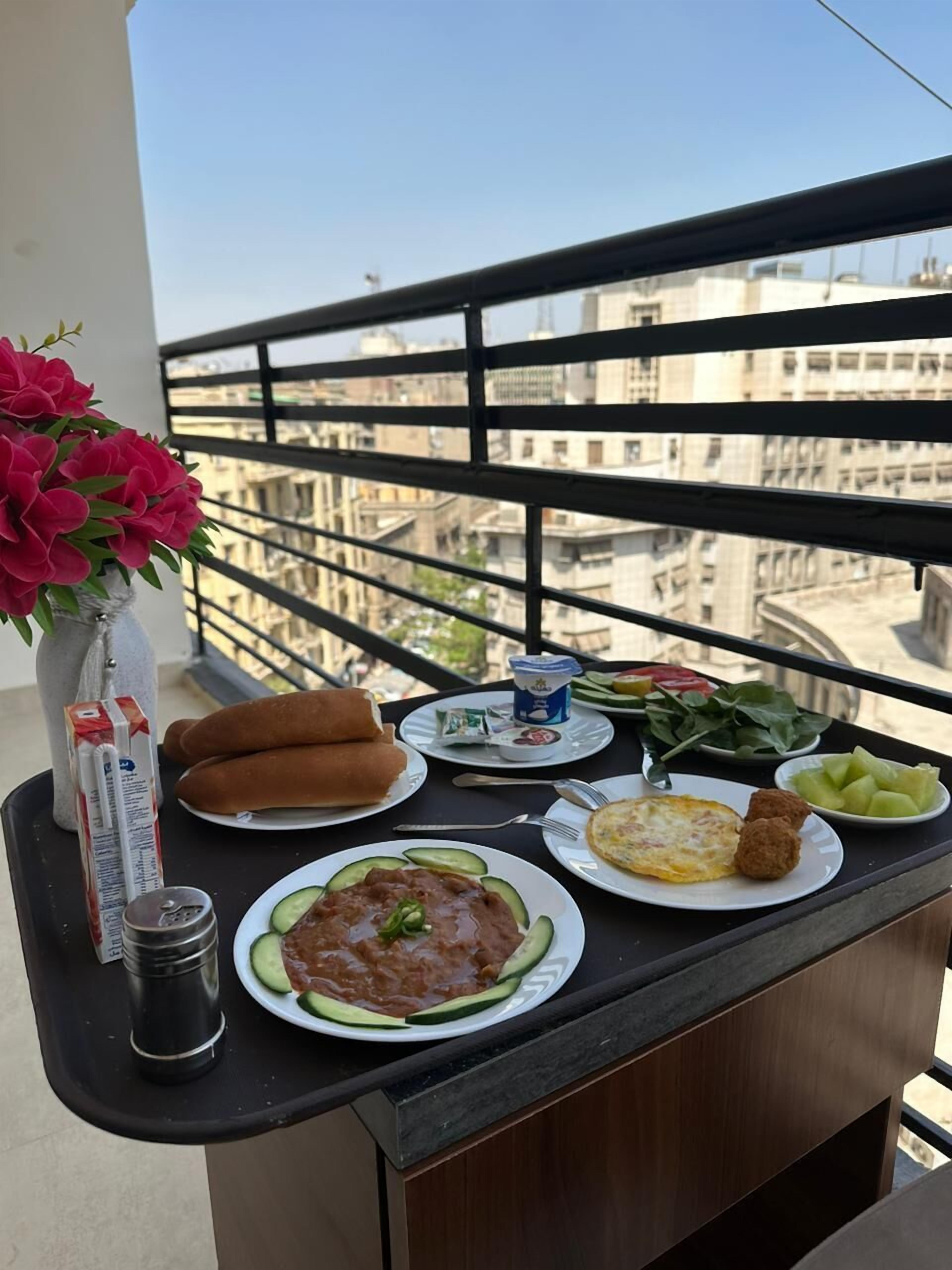 A balcony with a table set for a meal, including bread, beans, eggs, and vegetables.