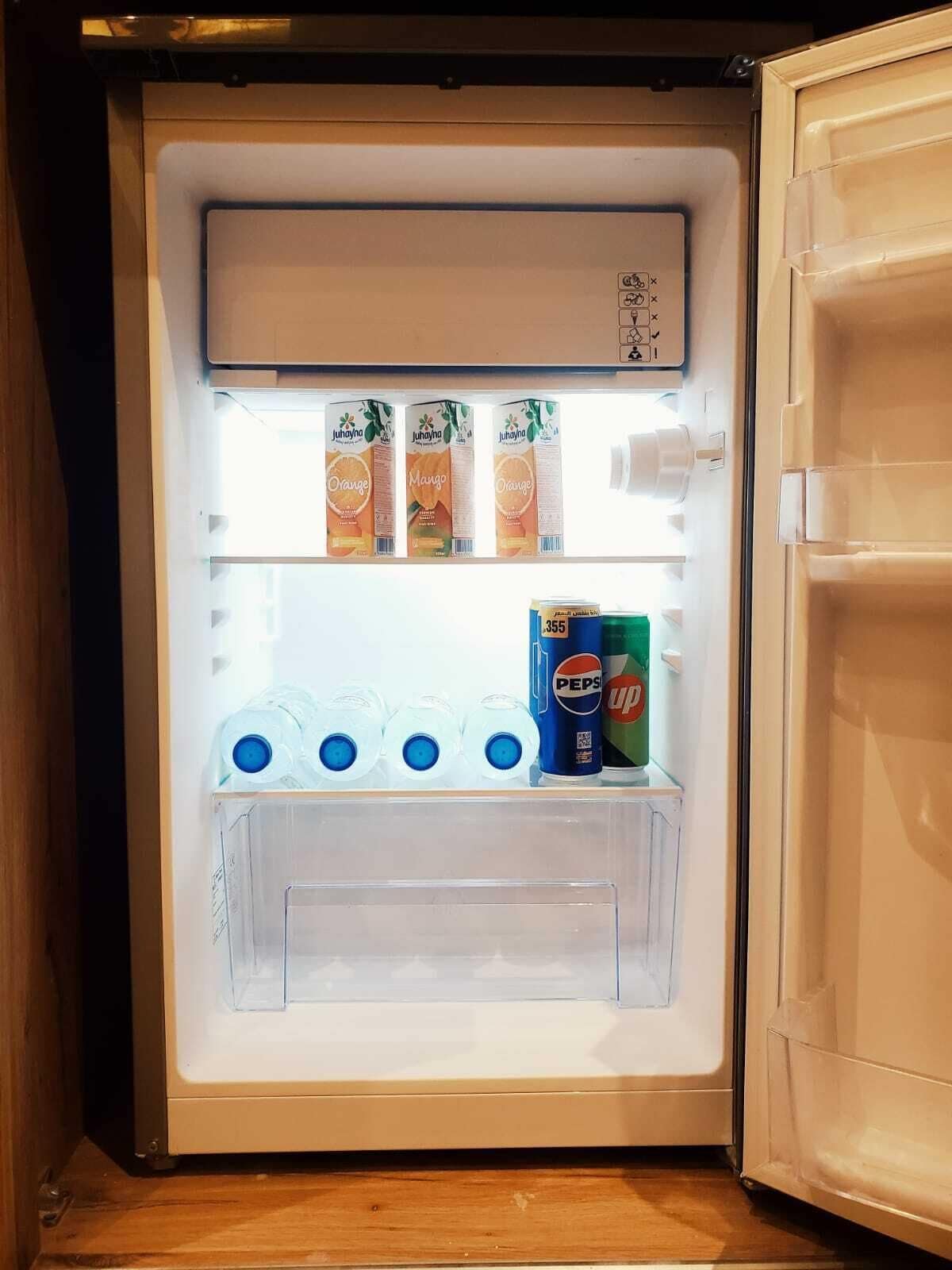 An open refrigerator with shelves containing juice cartons, water bottles, and a Pepsi can.