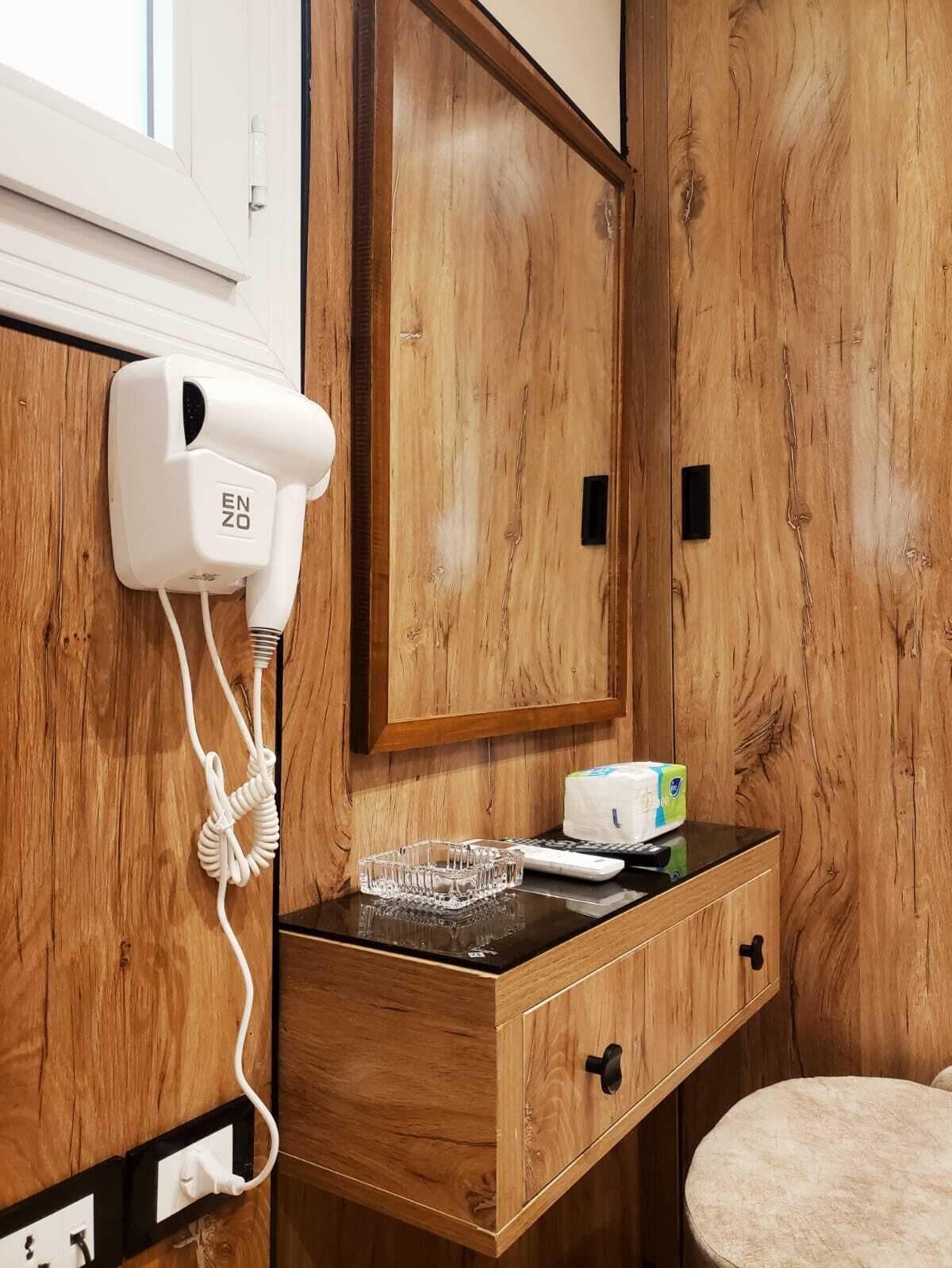 A wooden vanity with a hairdryer, a tissue box, and a glass ashtray on a black countertop.