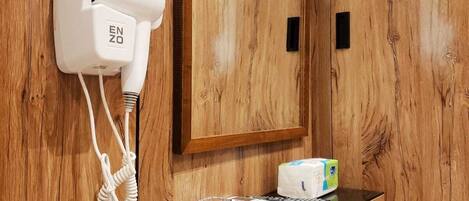 A wooden vanity with a hairdryer, a tissue box, and a glass ashtray on a black countertop.