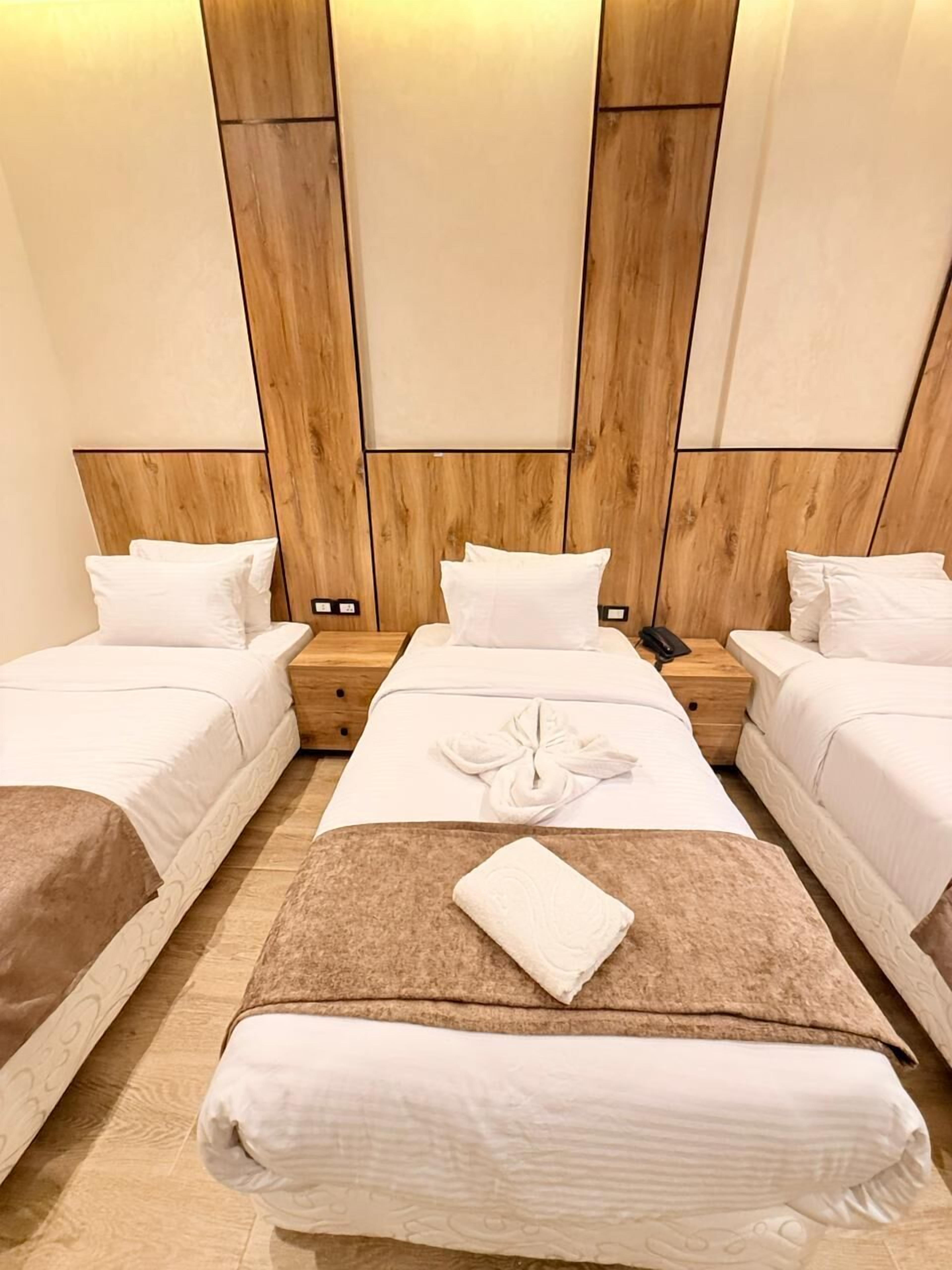 Habitación de hotel con dos camas individuales, una cama grande, paneles de cabecera de madera y alfombra marrón.