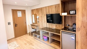 A modern hotel room with a wooden floor, a desk with a chair, a television, a small refrigerator, and a wooden cabinet. - white swan hotel (Cairo)