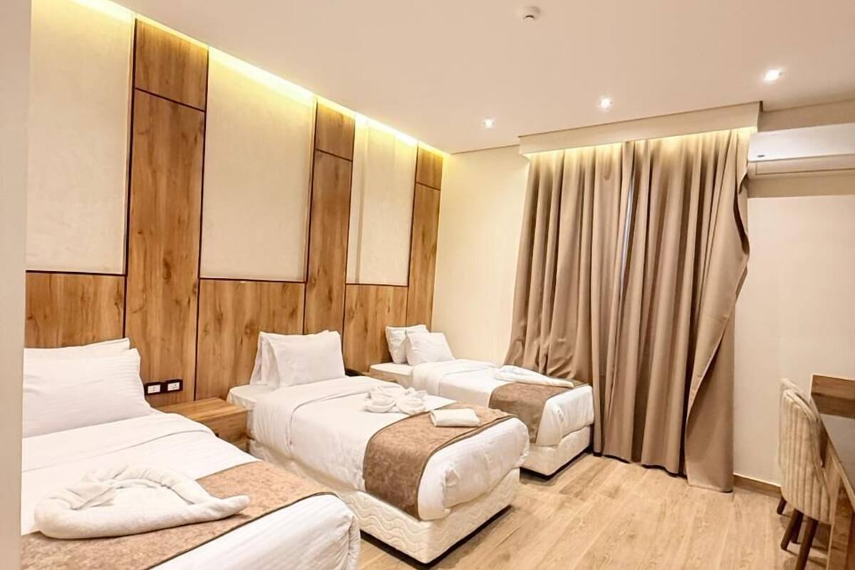 Una habitación de hotel con tres camas, paneles de madera en las paredes, un ventanal con cortinas y suelo de madera.