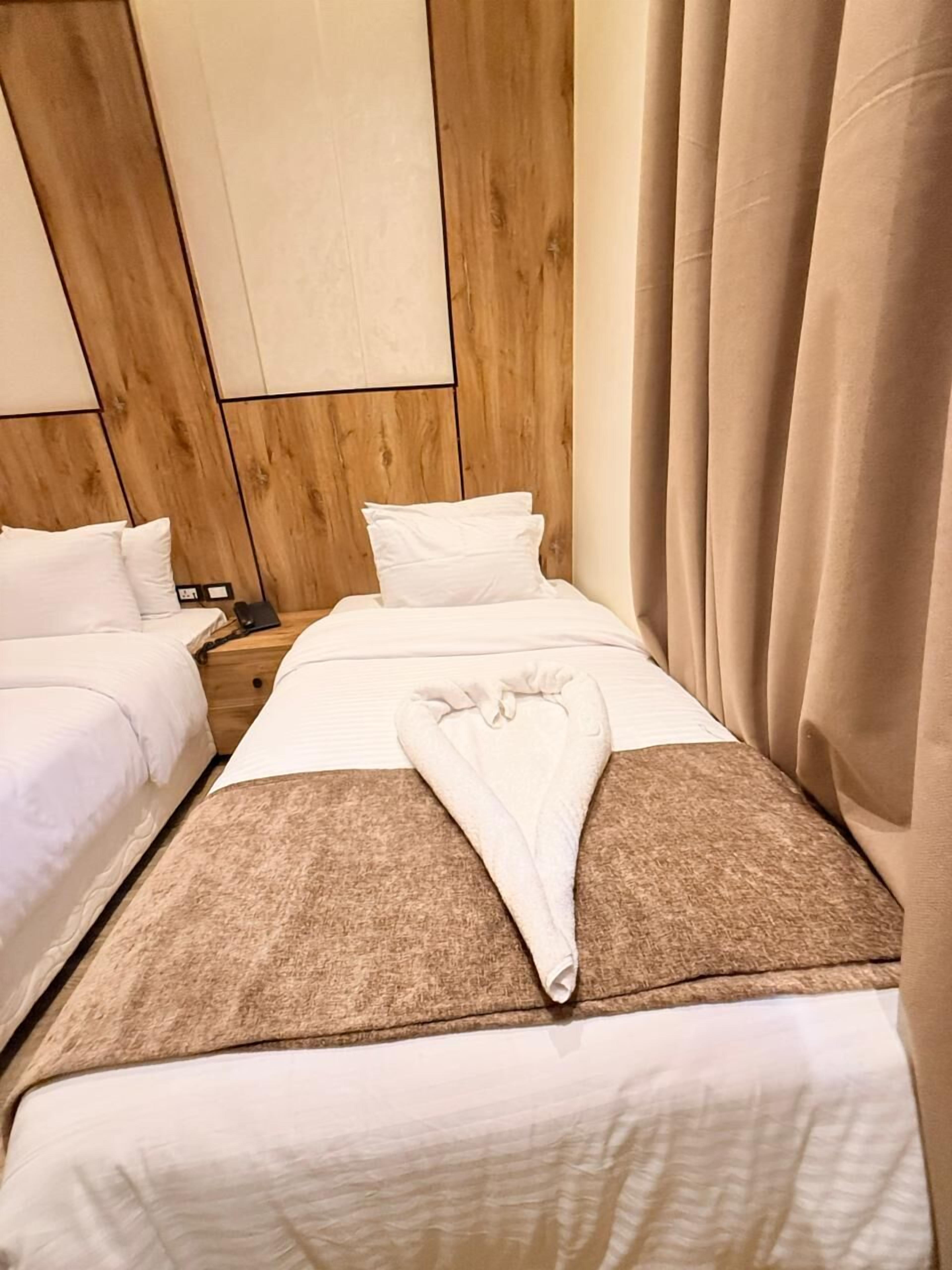 Une chambre d’hôtel avec deux lits, une tête de lit en bois, un plaid marron et un oreiller blanc.