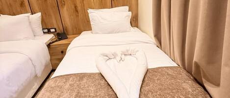 A hotel room with two beds, a wooden headboard, a brown throw blanket, and a white pillow.