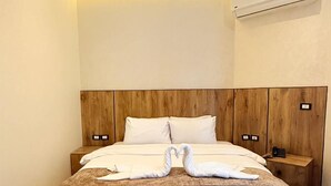 A modern hotel room with a large bed, wooden headboard, bedside tables, and an air conditioning unit. - white swan hotel (Cairo)