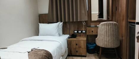 A bedroom with a bed, bedside table, chair, and an air conditioning unit.