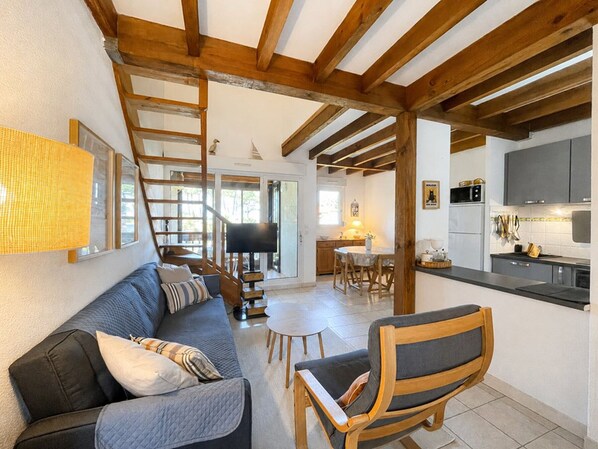 Un salon confortable avec un canapé, une chaise en bois, un escalier et un coin cuisine.