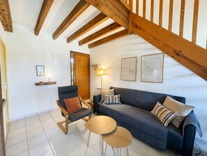A living room with a wooden ceiling, a sofa, a chair, a small table, and wall art. - Apartment, pets allowed - Pool and lake view (Soustons)
