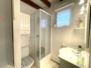 Une salle de bain avec une douche, des toilettes, un lavabo et une fenêtre avec un rideau.