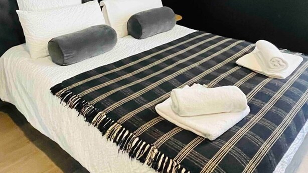 A modern bedroom with a tufted headboard, a striped bedspread, and neatly folded towels on the bed. - Le blue moon free parking 50 m historical center (Sarlat-la-Canéda)