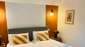 Un lit double avec une literie blanche et des oreillers à rayures, deux tables de chevet avec des lampes et un tableau encadré au mur.
