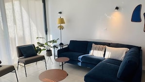 A modern living room with a dark blue sofa, a small round table, a chair, and a floor lamp.