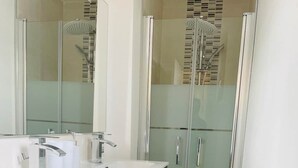 A modern bathroom with a glass shower enclosure, a white sink with a mirror, and a dark-colored cabinet. - Le logis de la lanterne (Sarlat-la-Canéda)