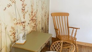 A room with a wooden floor, a wooden chair, a small table, and a wall with a floral pattern. - Le logis de la lanterne (Sarlat-la-Canéda)