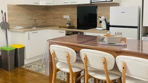 A modern kitchen with white cabinets, a wooden countertop, a microwave, a refrigerator, and a dining area with wooden chairs. - Le logis de la lanterne (Sarlat-la-Canéda)